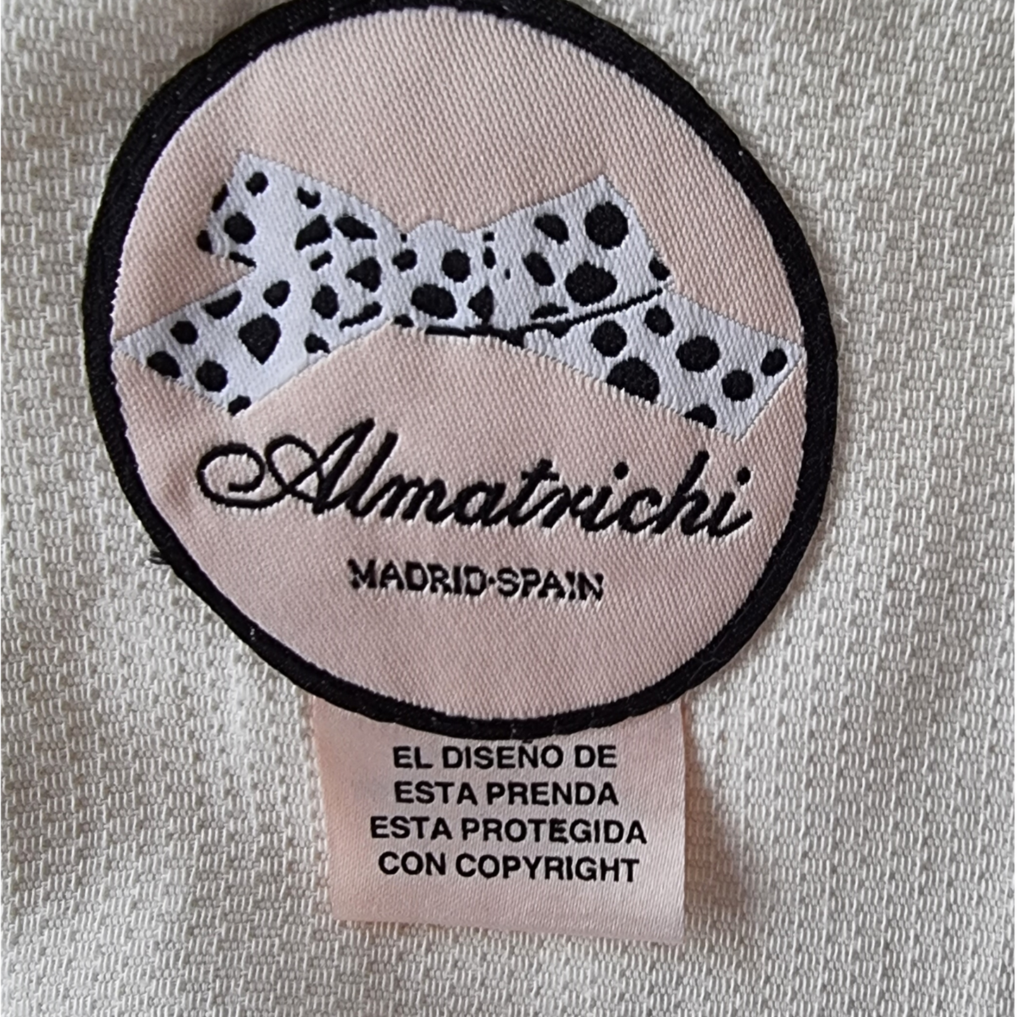Fabric label with a bow design and 'Almatrichi Madrid Spain' text on a textured background