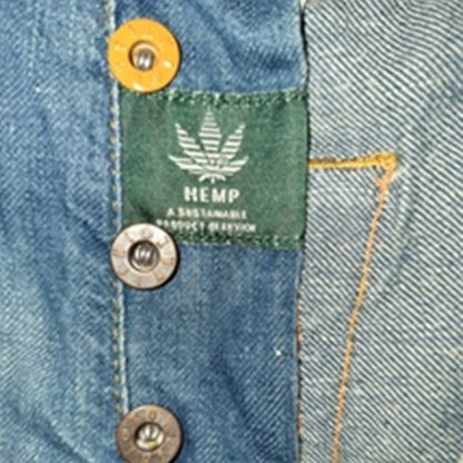 Close-up of a blue denim garment showing a green fabric label with a white hemp leaf and the text 'HEMP A SUSTAINABLE PRODUCT REVISION', plus brass and silver buttons.