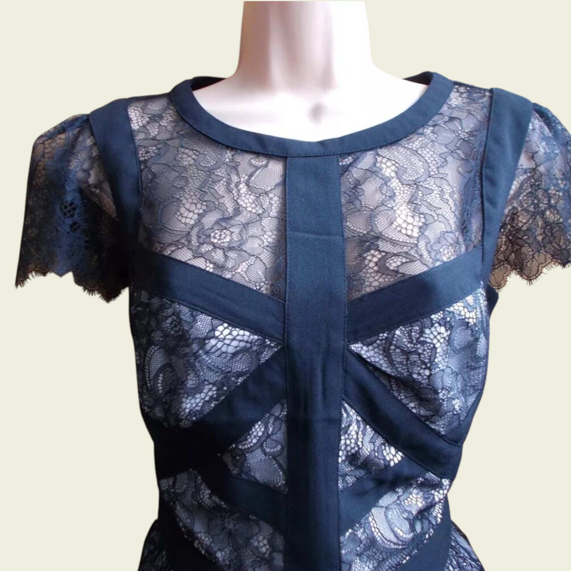 Black lace dress on a mannequin against a plain background