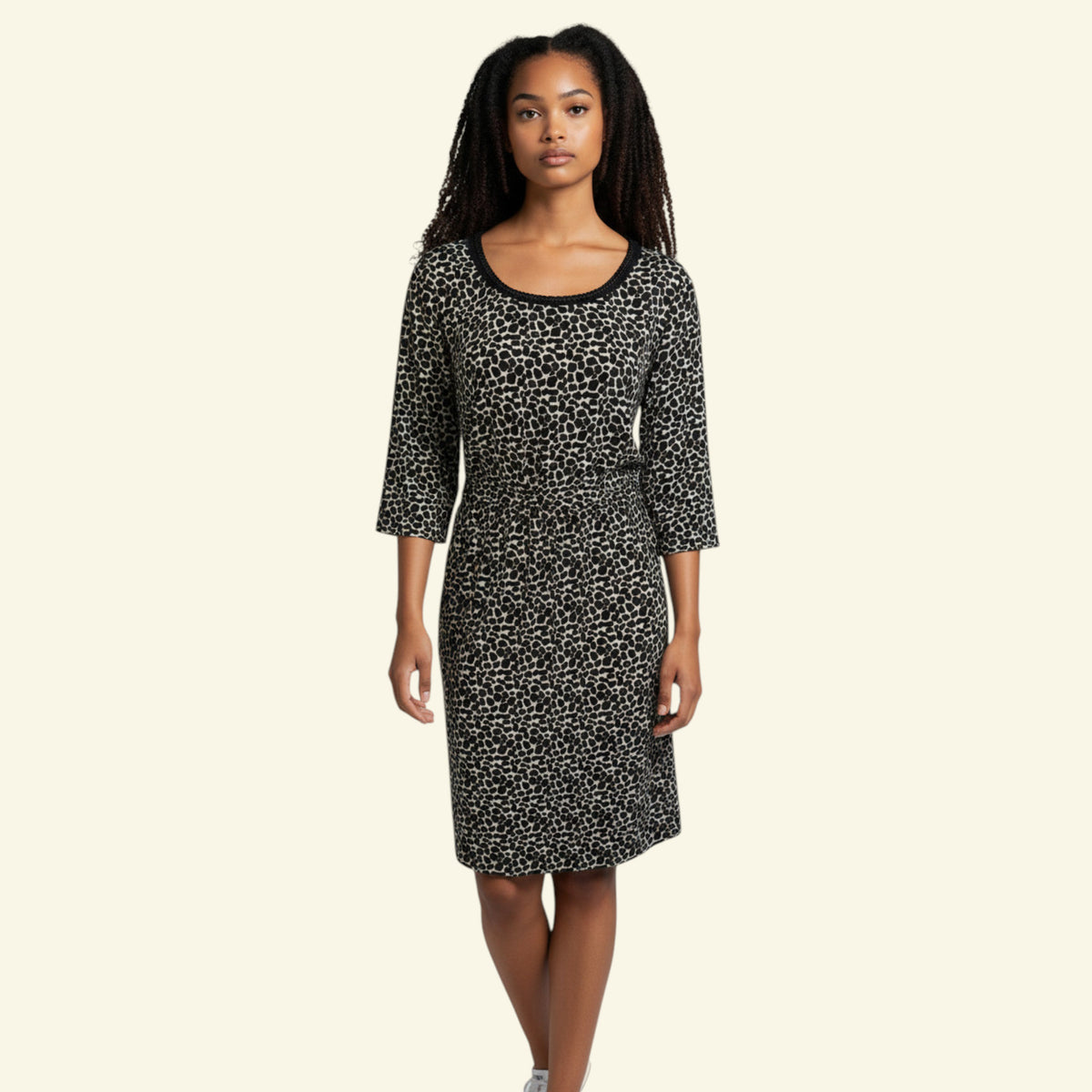 A woman modeling a black and white patterned knee-length dress with three-quarter sleeves and a scoop neckline, set against a solid cream background.
