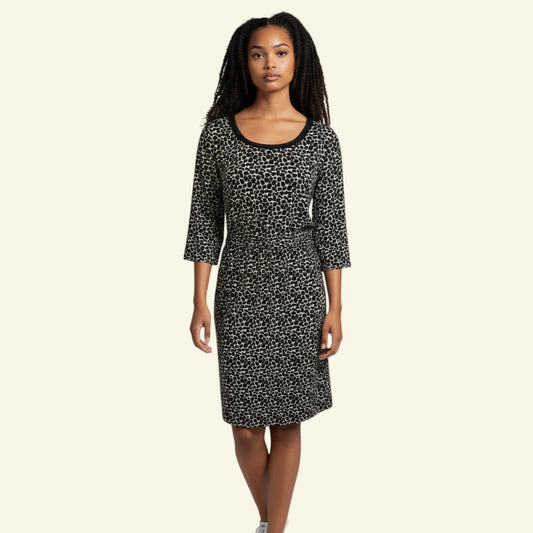 A woman modeling a black and white patterned knee-length dress with three-quarter sleeves and a scoop neckline, set against a solid cream background.