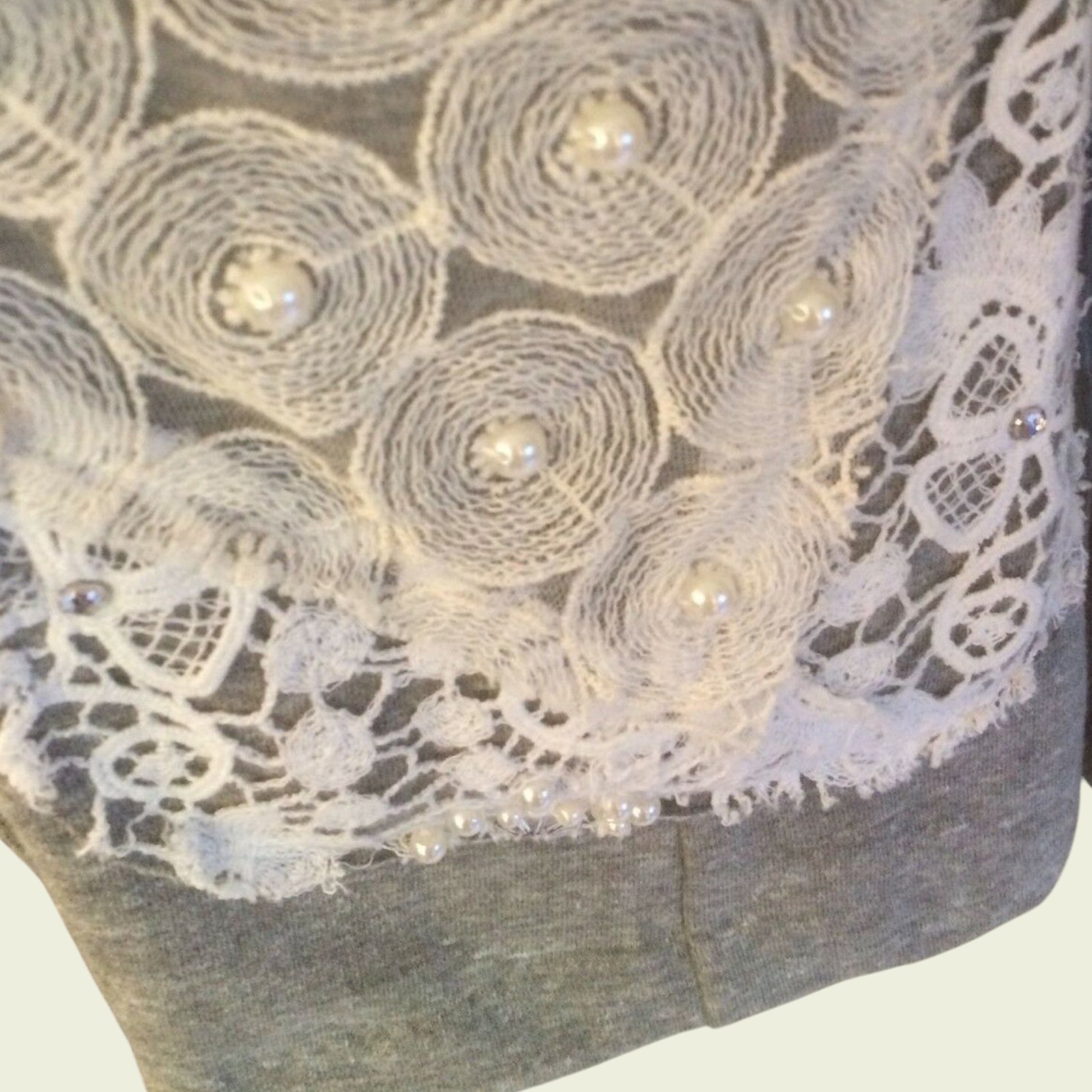 Close-up of a gray garment with intricate white lace and pearl embellishments.