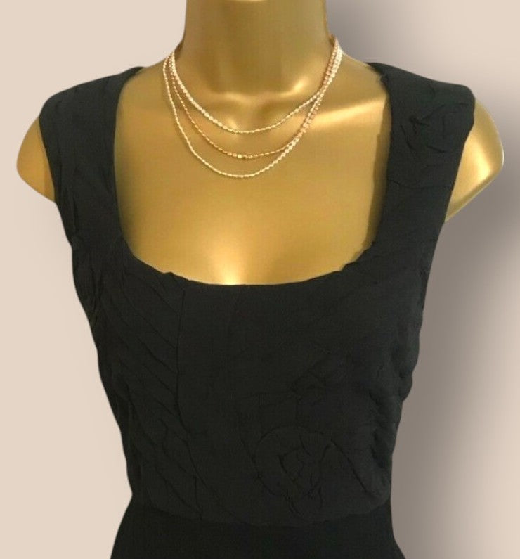 Black sleeveless top on a mannequin with a gold necklace against a plain background