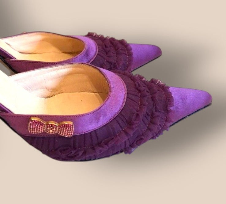 Purple high-heeled shoes with ruffles and a bow on a light background