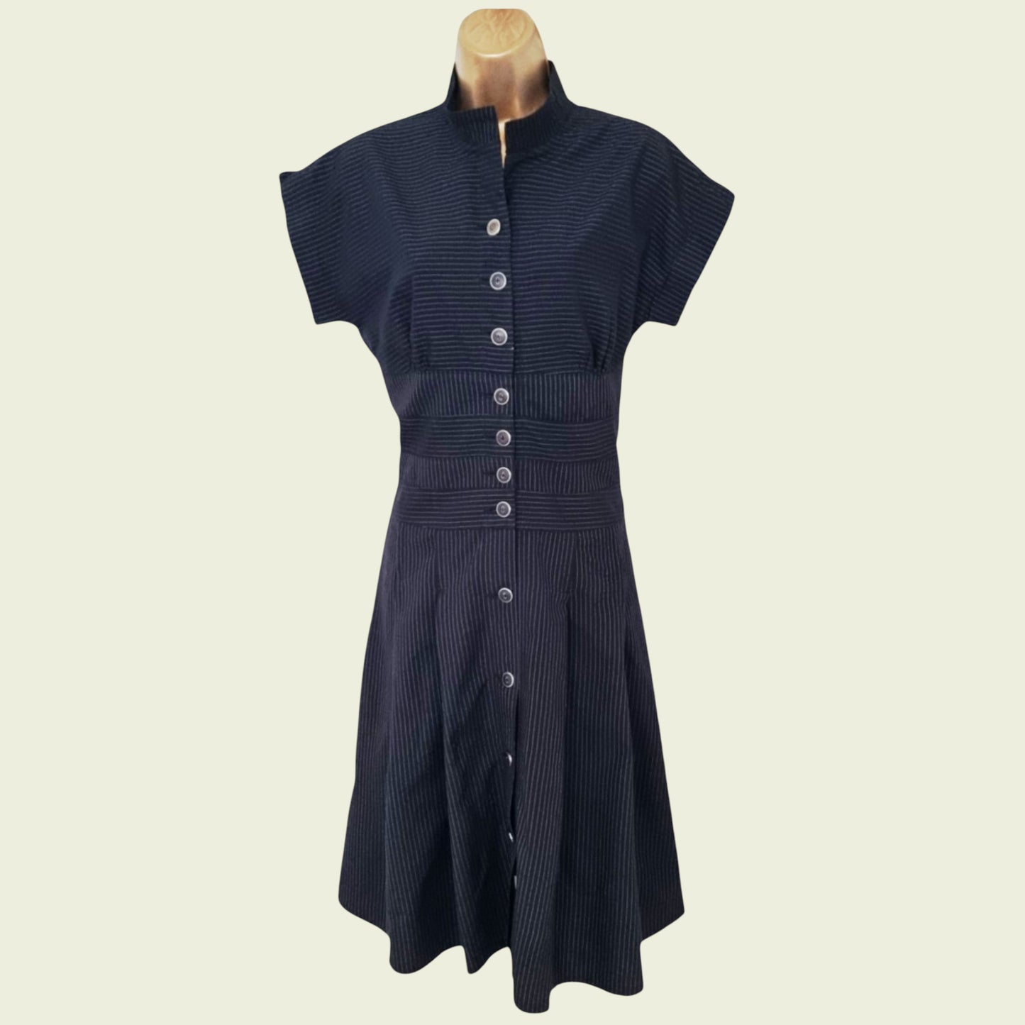 Navy dress with button details on a mannequin against a beige background