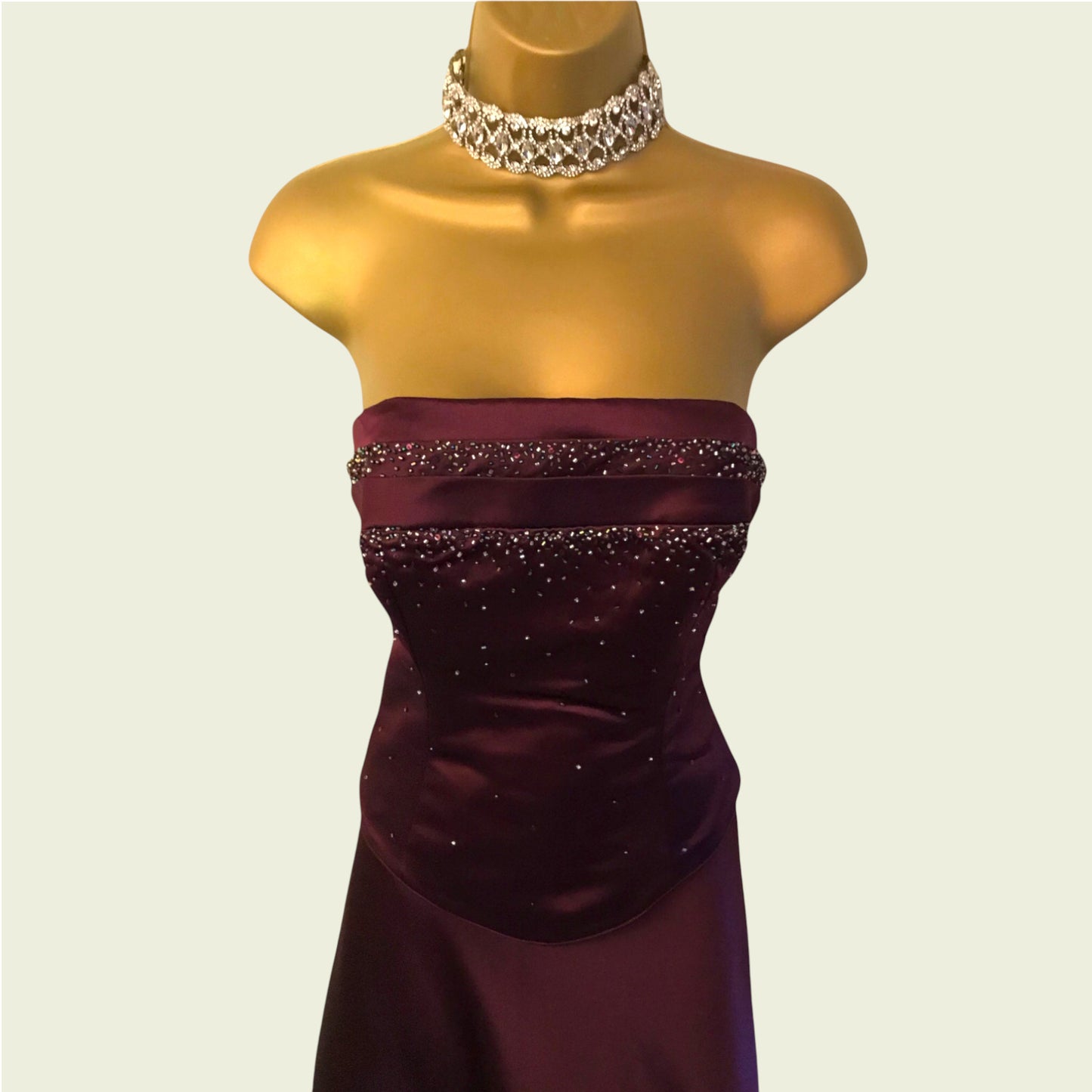 Burgundy strapless dress with beading on a mannequin against a plain background