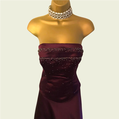 Burgundy strapless dress with beading on a mannequin against a plain background