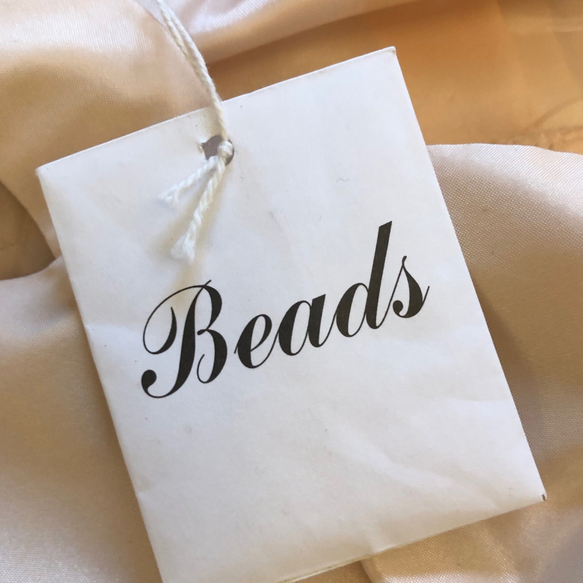 White drawstring bag labeled 'Beads' on a beige fabric background