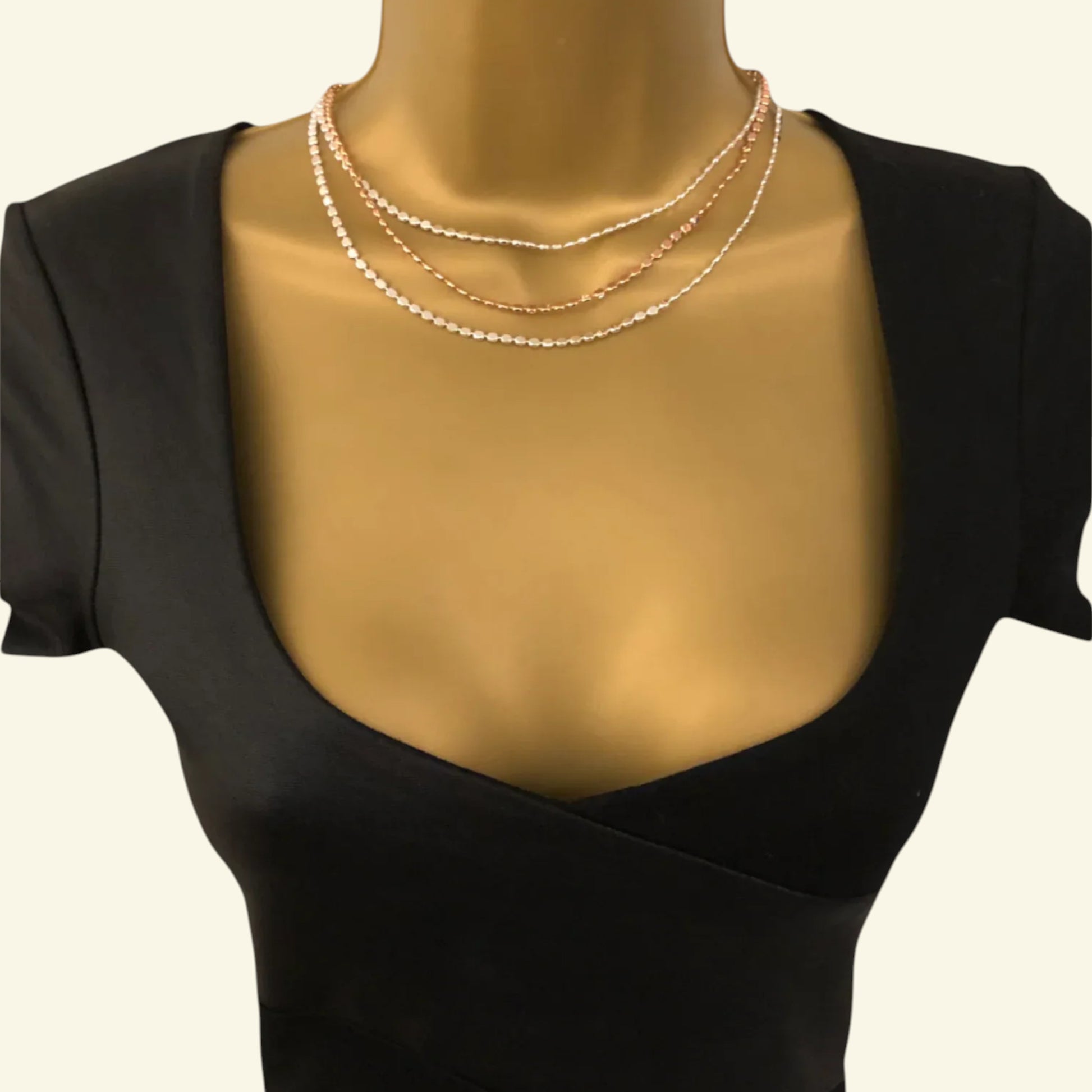Mannequin wearing a black top with a pearl necklace on a plain background