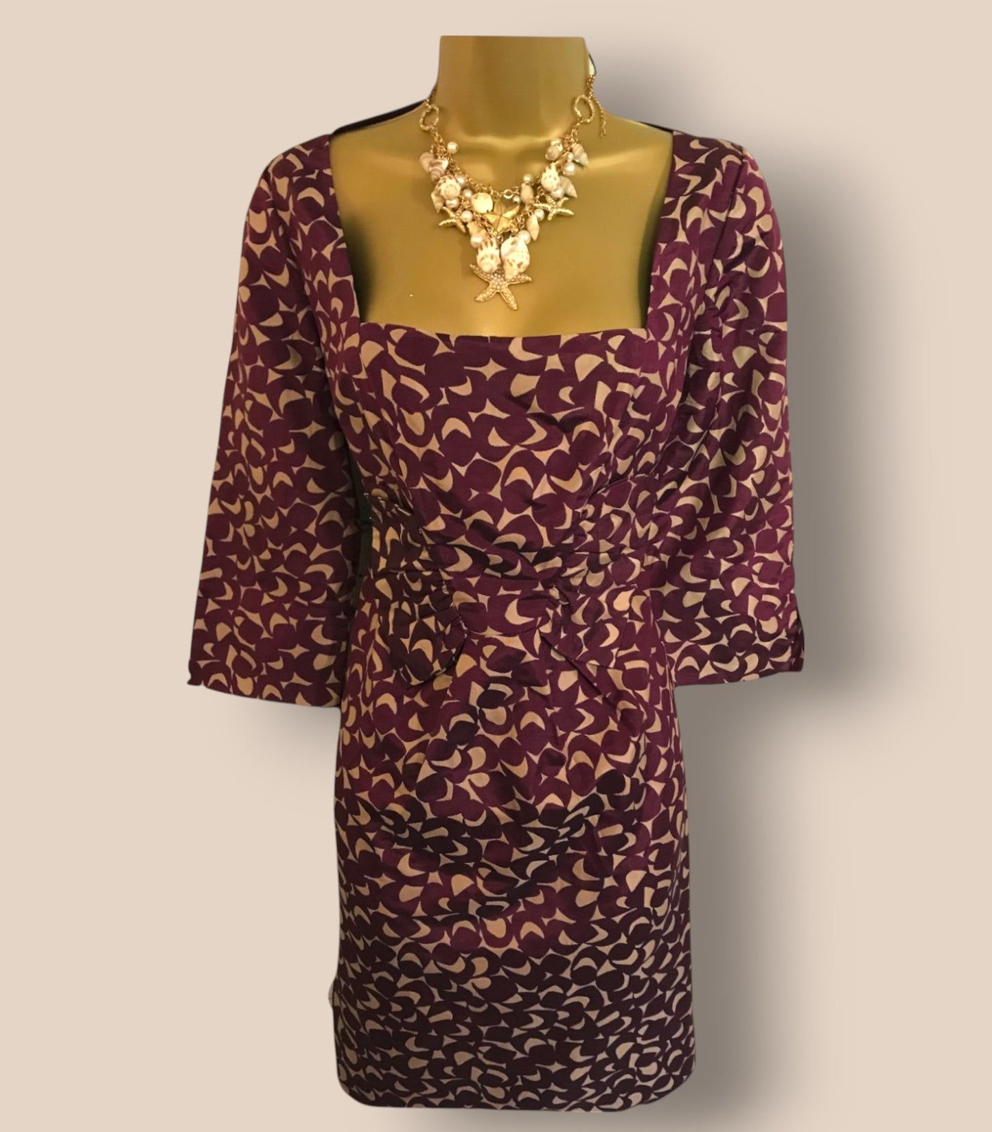 Purple patterned dress on a mannequin with a gold necklace against a beige background