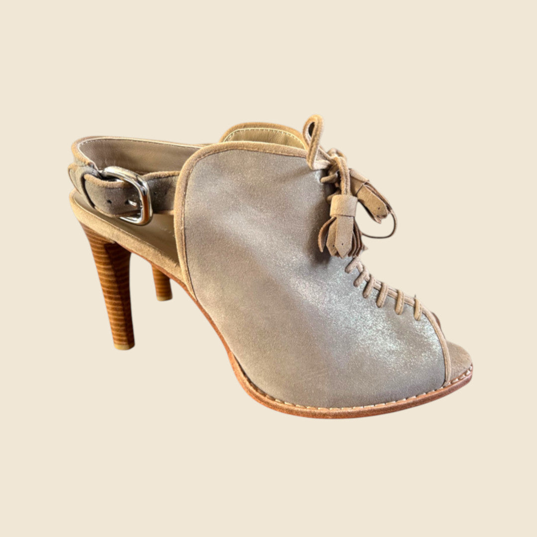 Beige high-heeled shoe with tassel on a beige background
