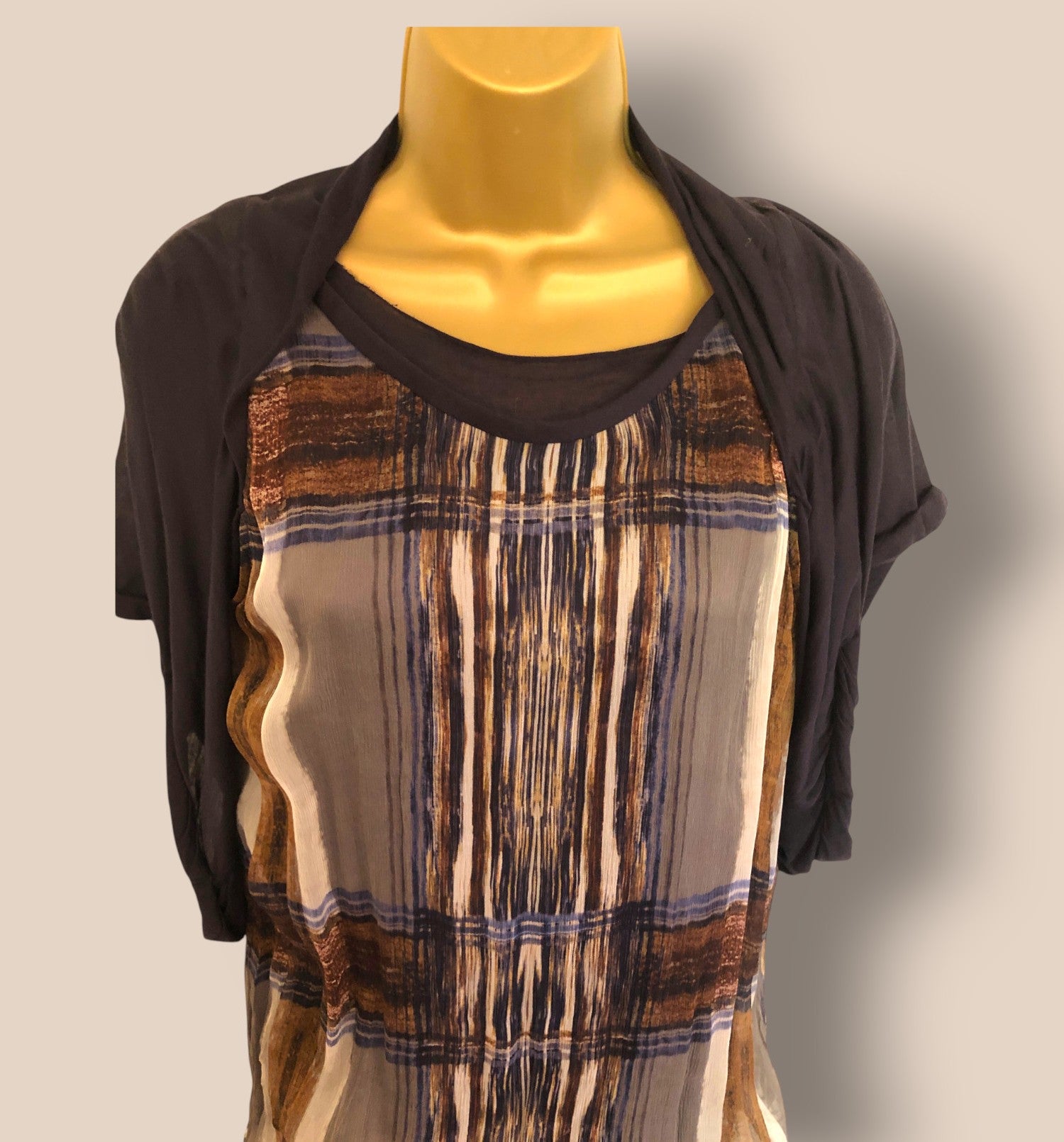 Mannequin wearing a brown and beige patterned dress with a black cardigan on a plain background