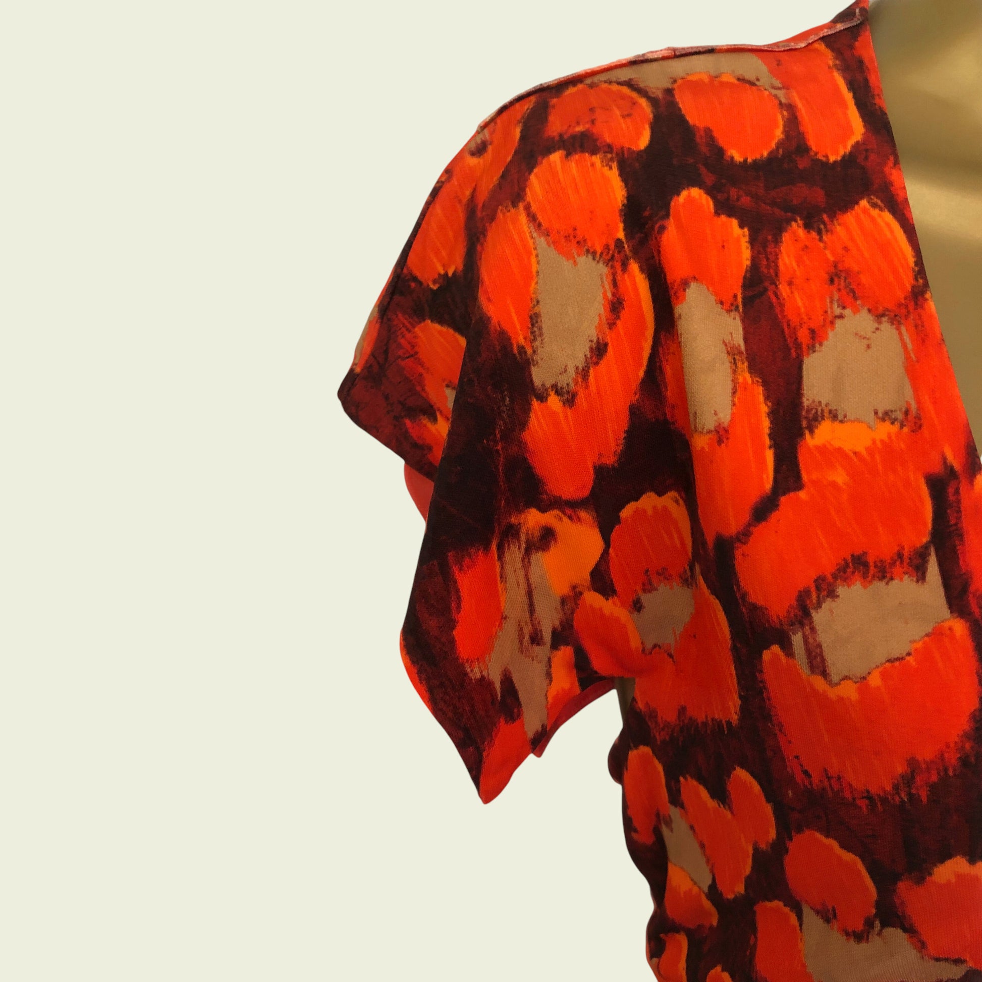 Model showing sleeve detail of bright orange and black dress on beige background