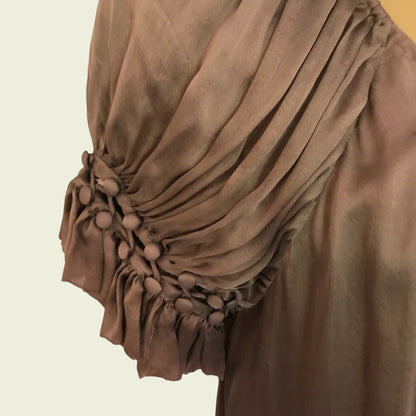 Close-up of a brown garment with pom-pom detailed sleeve on a beige background