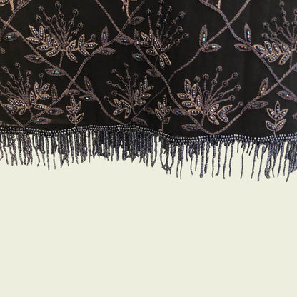 Close-up of a black fabric with intricate beadwork and fringes on a beige background