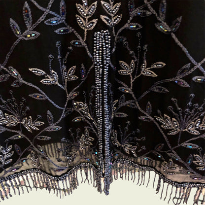 Close-up of an intricately beaded and embroidered fabric with floral patterns on a dark background.