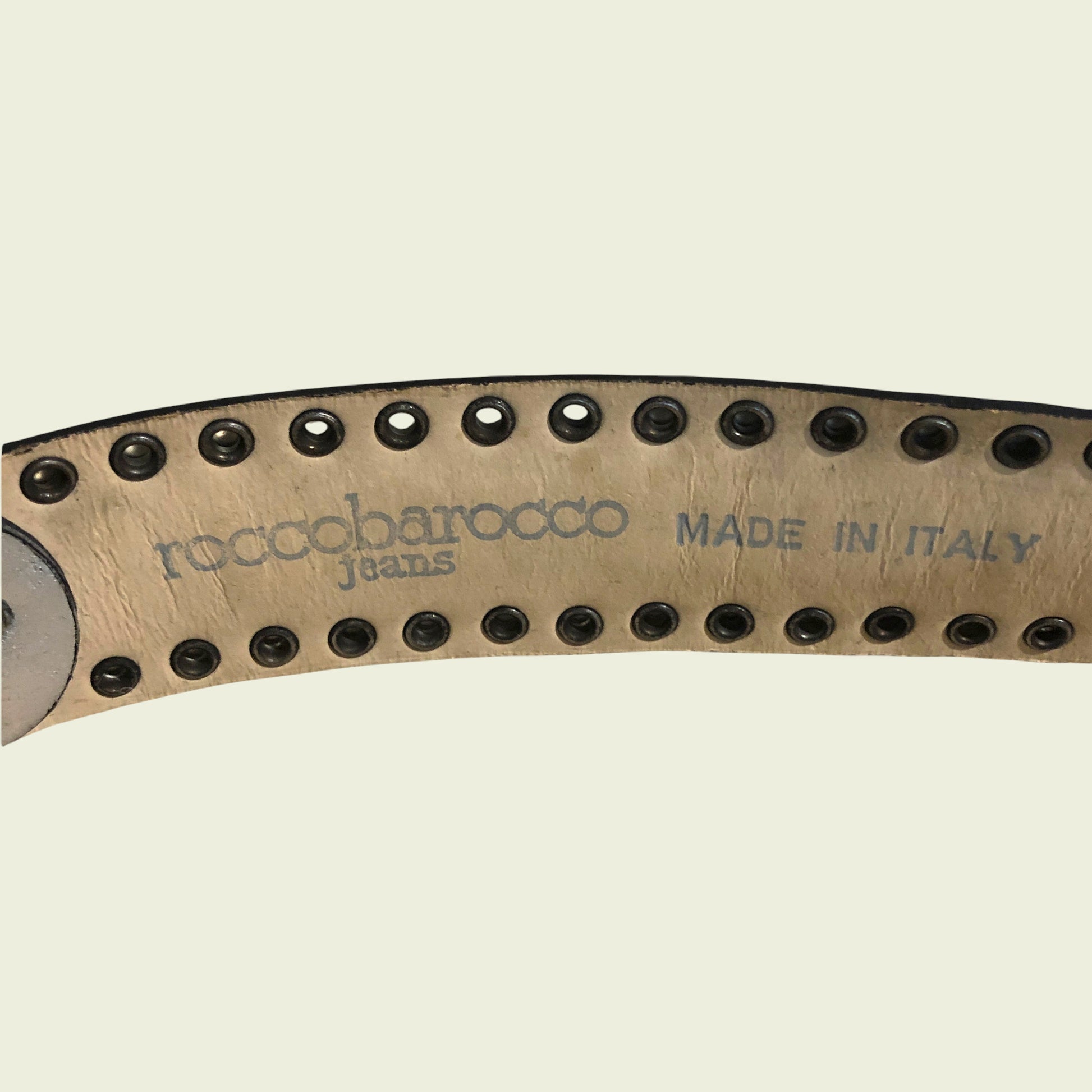 Close-up of a belt with 'roccobarocco jeans' branding and 'Made in Italy' text on a beige background.