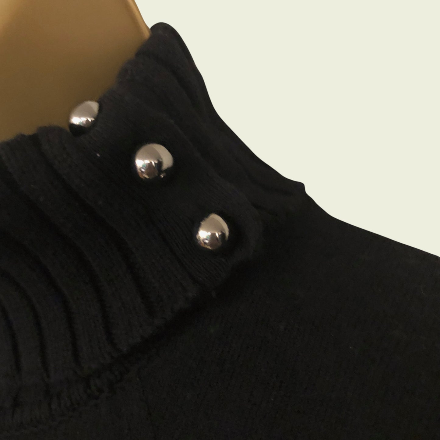 Close-up of a black garment with silver buttons on a beige background