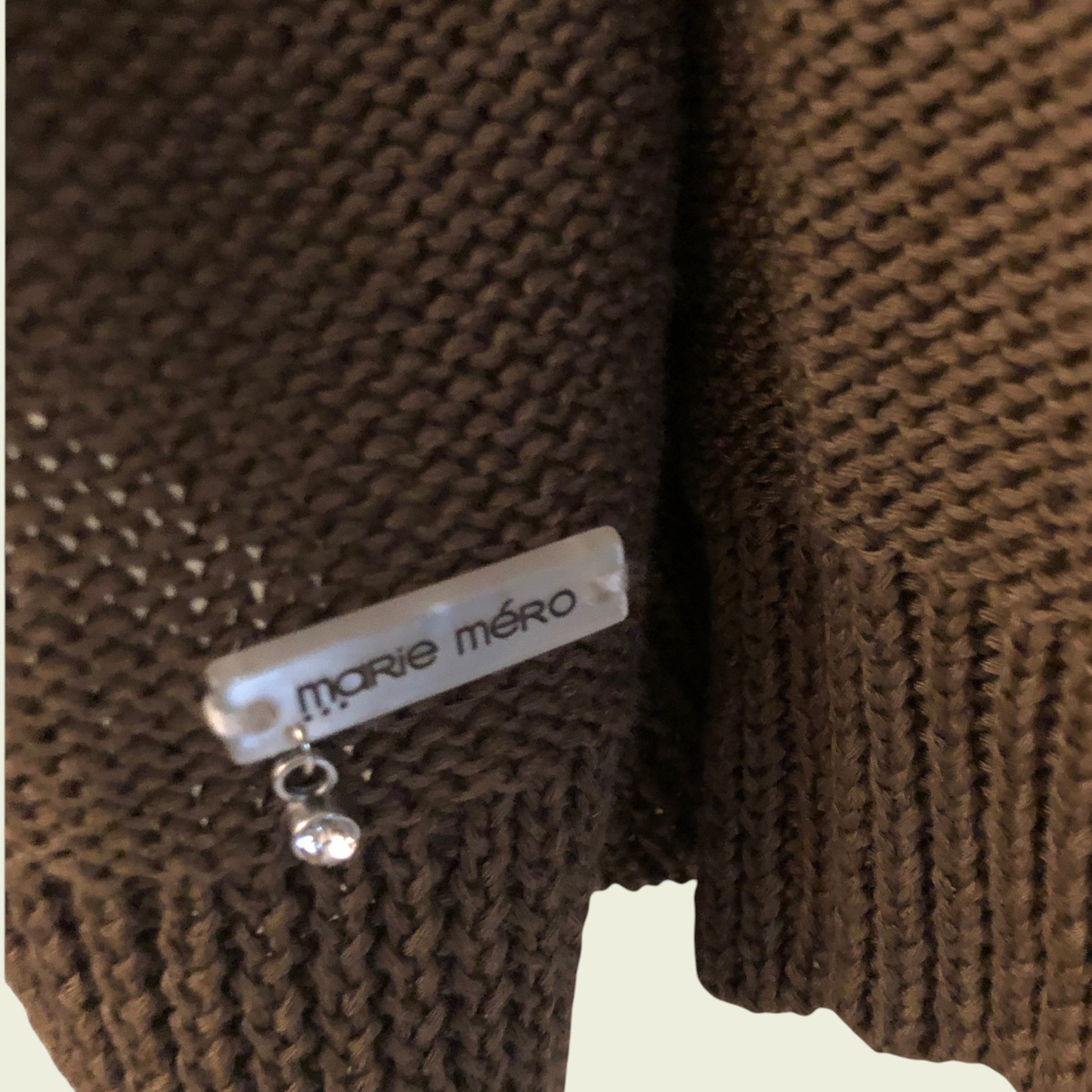Brown knitted sweater with 'Marie Méro' label on a beige background