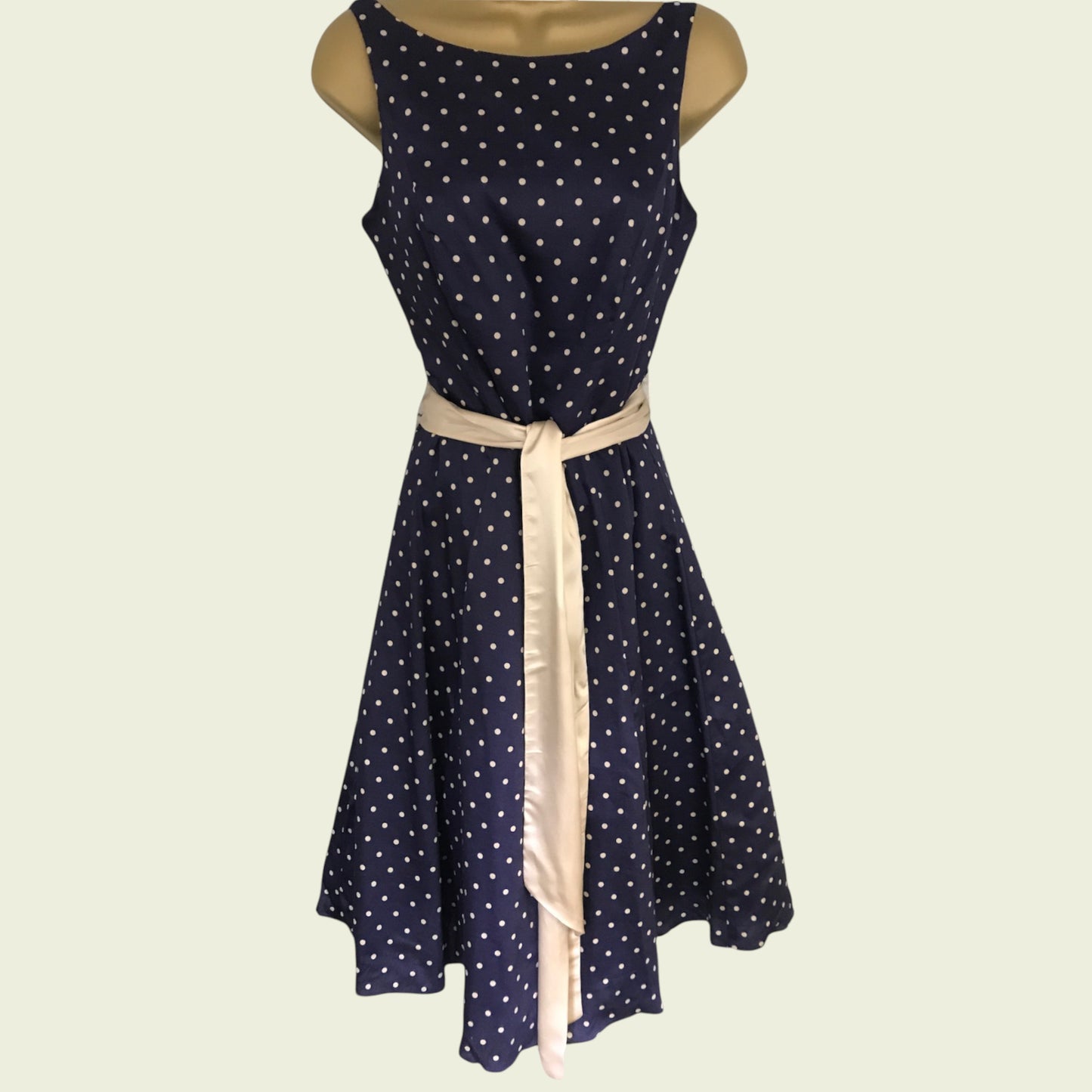 Navy blue dress with white polka dots and a beige ribbon on a light beige background