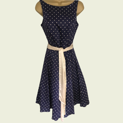 Navy blue dress with white polka dots and a beige ribbon on a light beige background