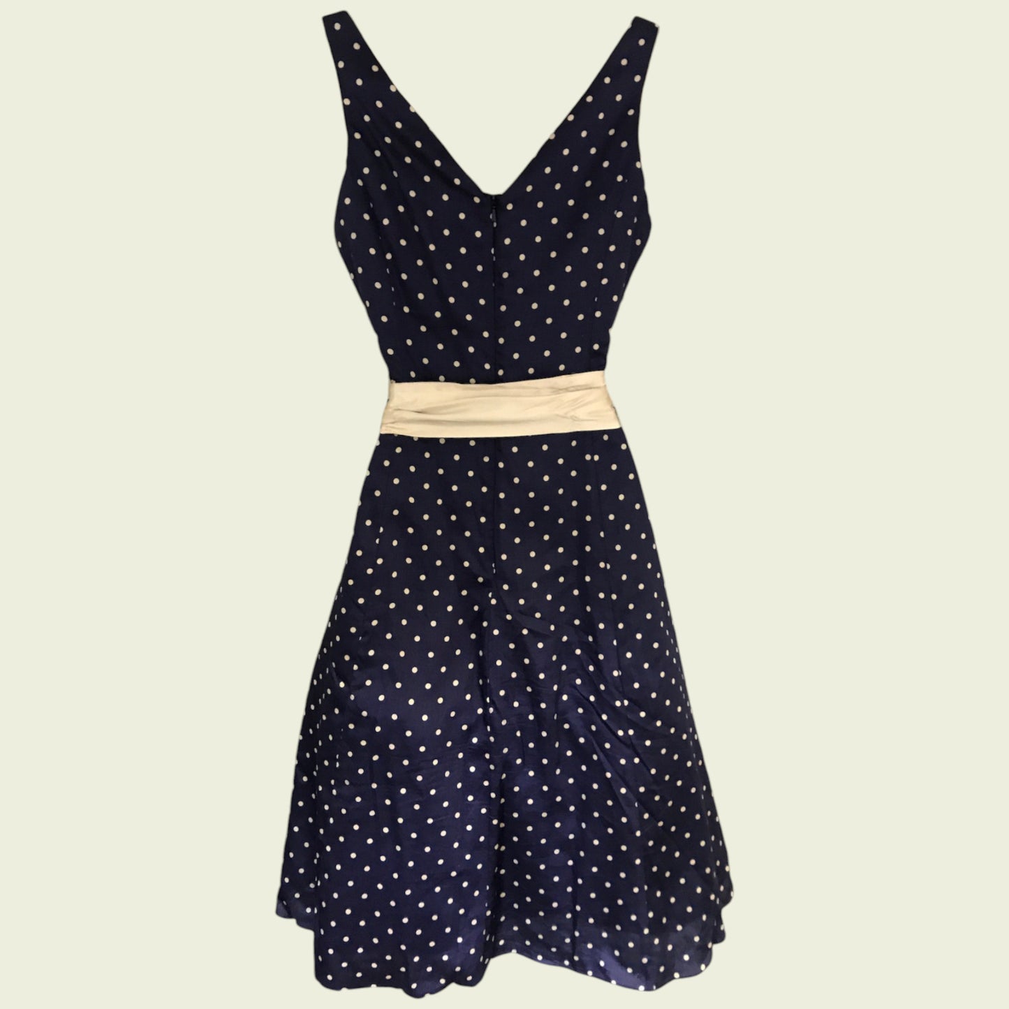 Navy polka dot dress with a beige belt on a beige background