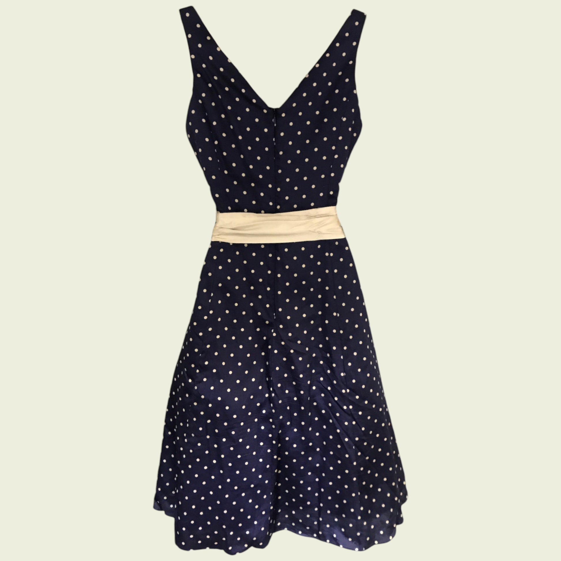 Navy polka dot dress with a beige belt on a beige background