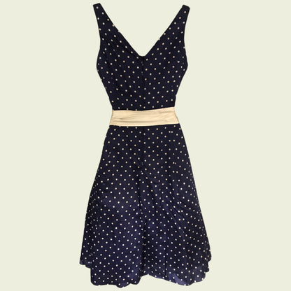 Navy polka dot dress with a beige belt on a beige background