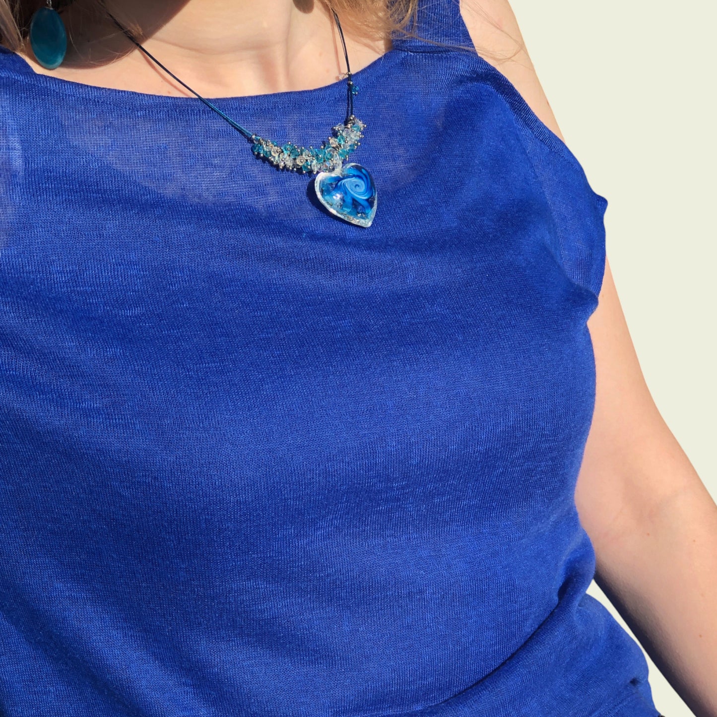 Person wearing a blue top with a heart-shaped pendant necklace.