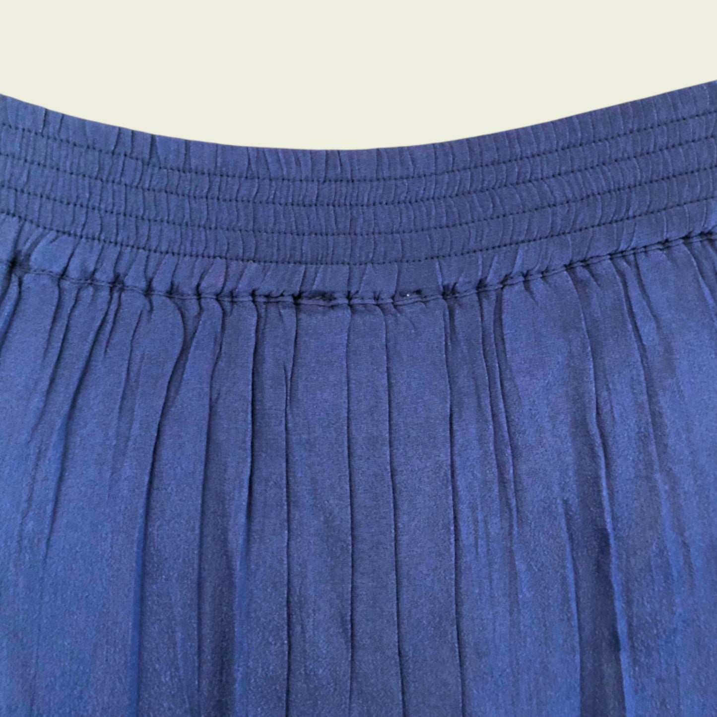 Waistband of blue pleated mini skirt on beige background