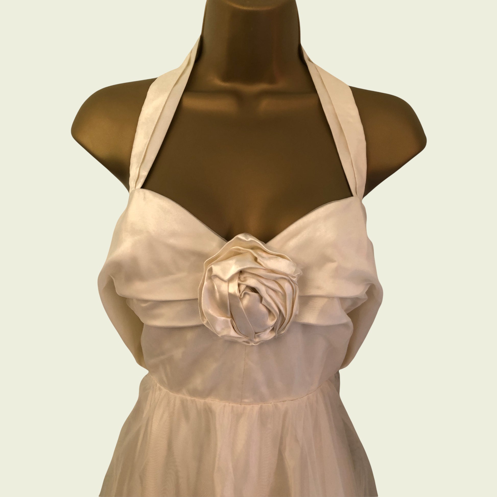 Mannequin wearing cream organza prom dress with rose detail on beige background