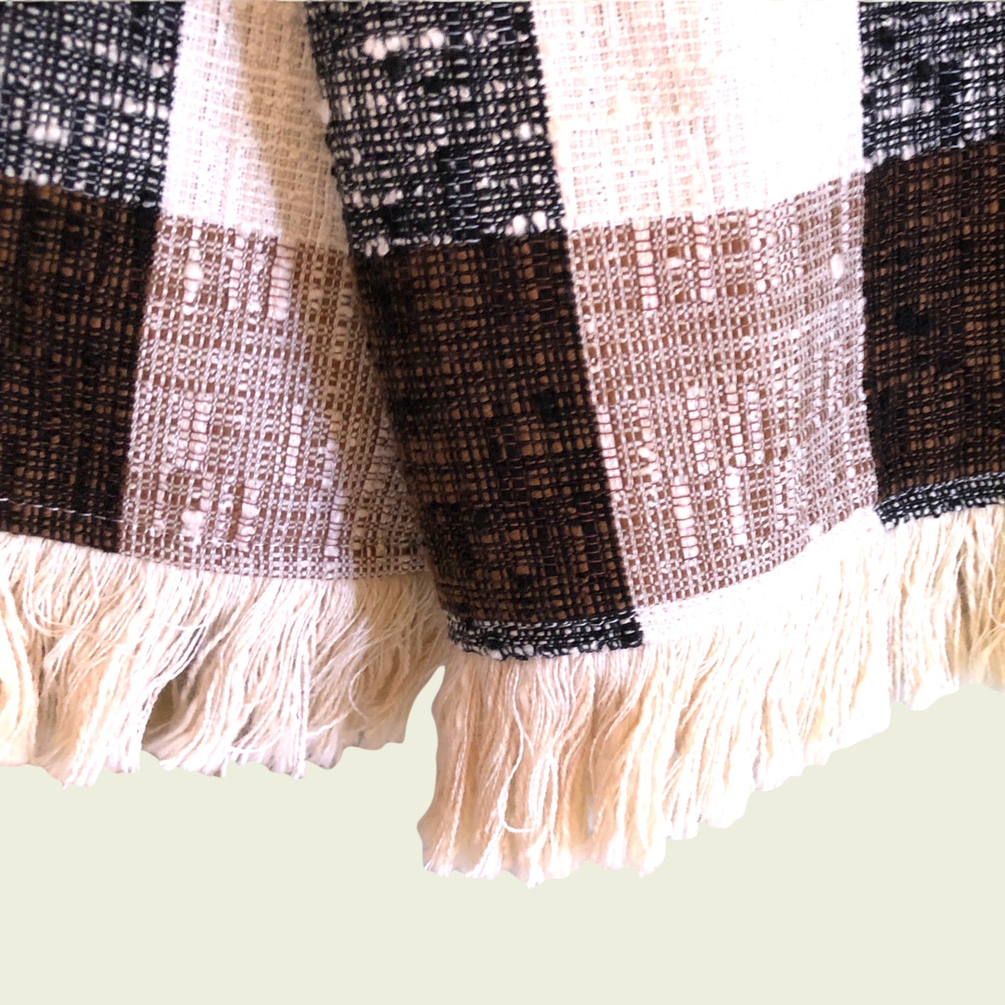 Close-up of a plaid fabric with fringes on a light green background