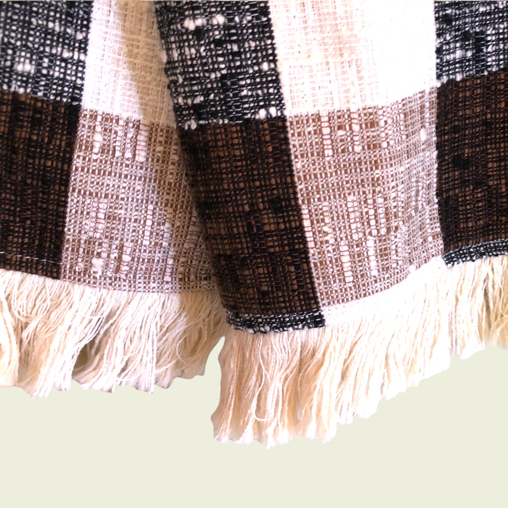 Close-up of a plaid fabric with fringes on a light green background