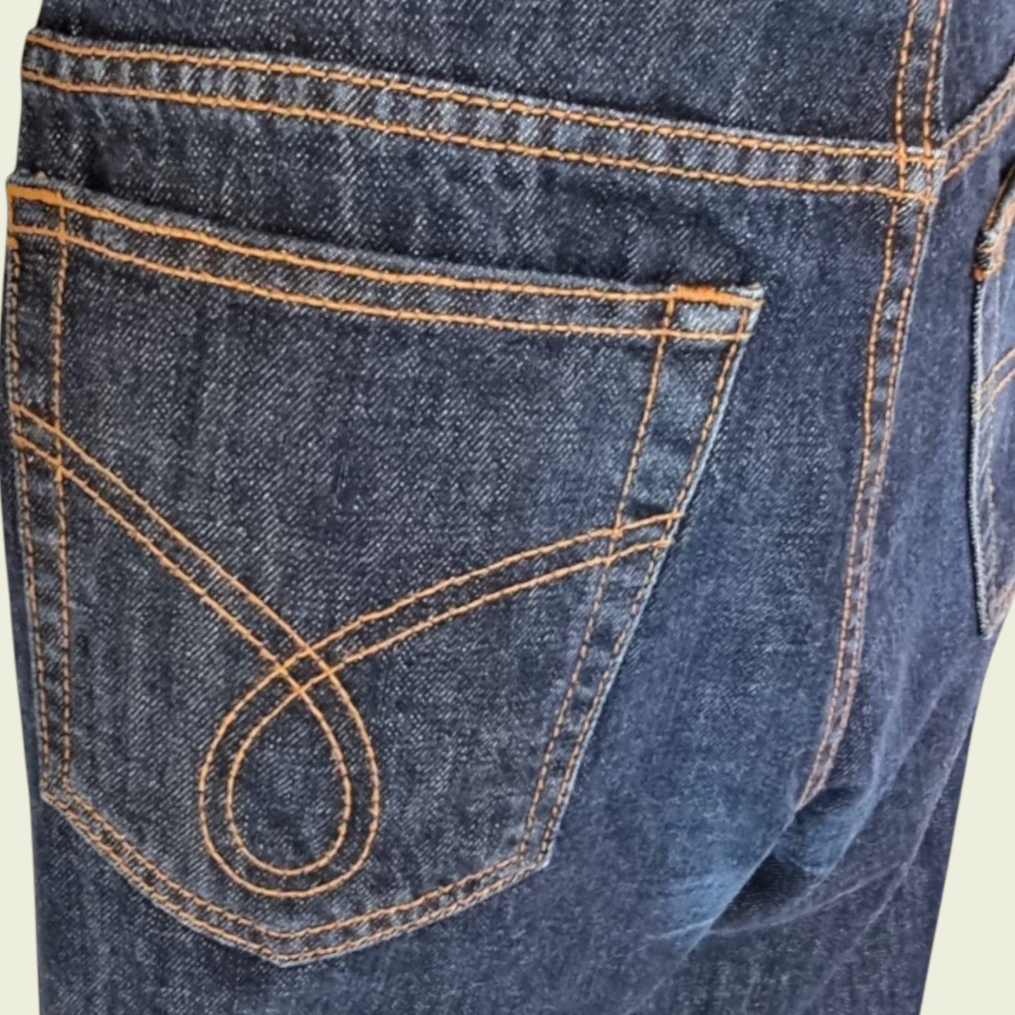 Close-up of a blue denim pocket with orange stitching on a beige background