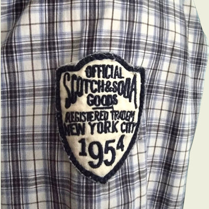 Plaid shirt with a patch reading 'Official Scotch & Soda Goods, Registered Trade New York City 1954'.