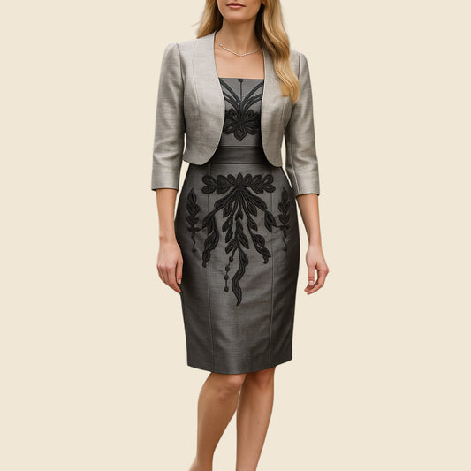 Woman wearing a gray bollero and black dress with embroidery on a beige background