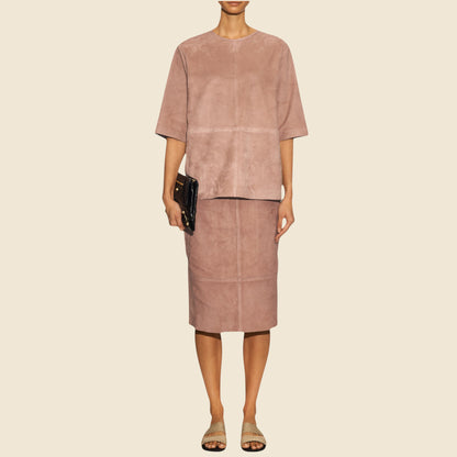 Person wearing a mauve outfit with a skirt and top on a beige background
