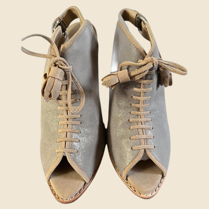 Pair of metallic beige open-toe shoes with beige laces on a beige background