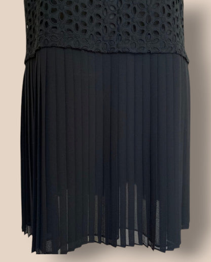Black dress with a textured top and pleated skirt on a beige background