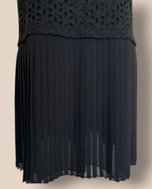 Black dress with a textured top and pleated skirt on a beige background