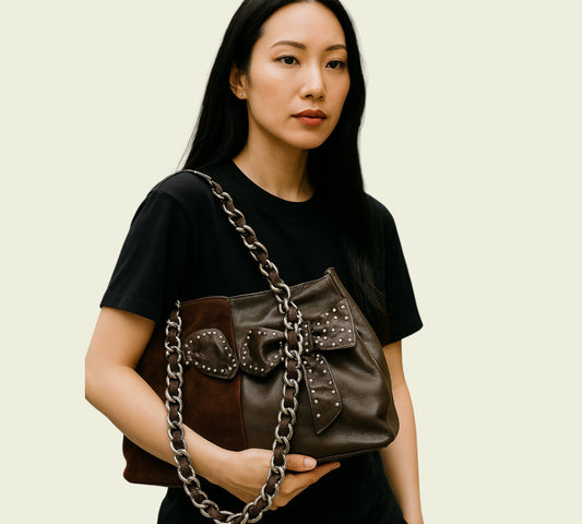 Woman holding a brown leather handbag with chain strap against a beige background