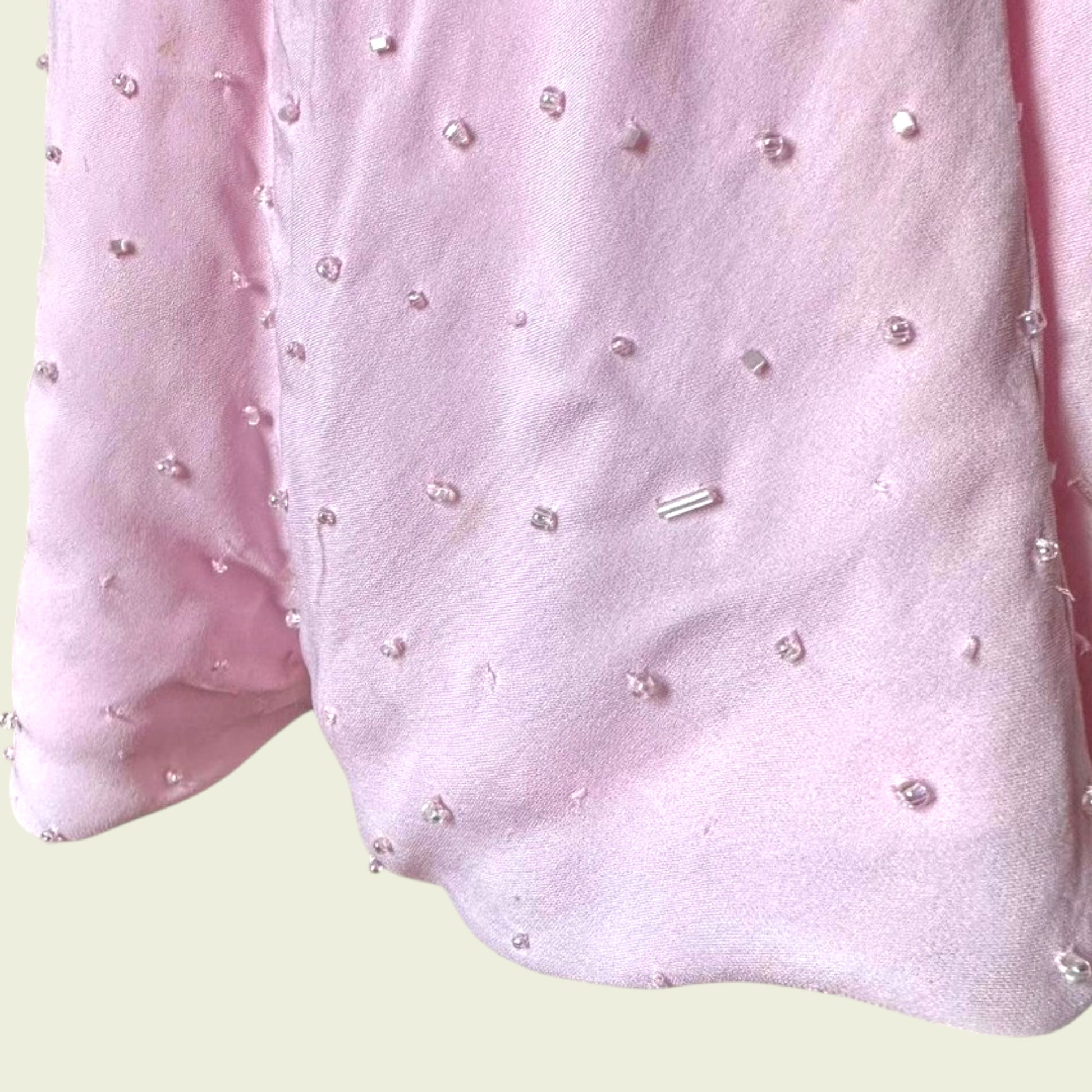 Close up of hemline on pink dress with bead embellishments on a light green background