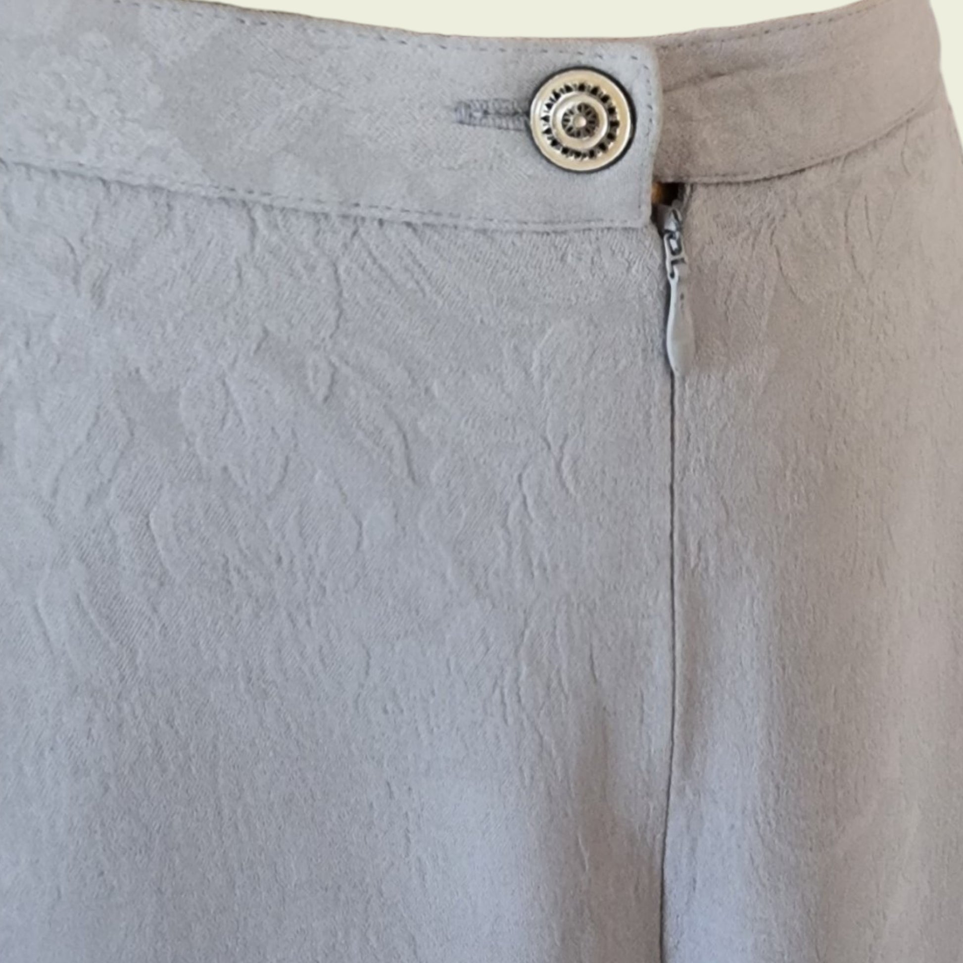 Close-up of light gray skirt with a button and zipper detail.