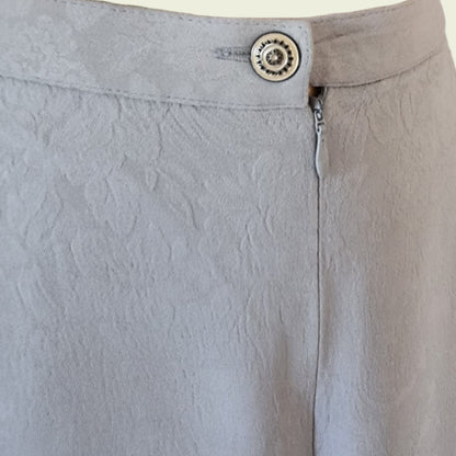 Close-up of light gray skirt with a button and zipper detail.