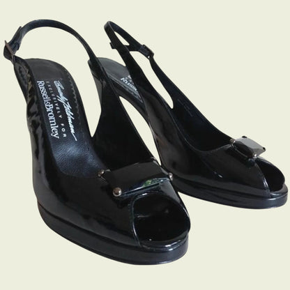 Black patent leather shoes with a bow detail on a beige background