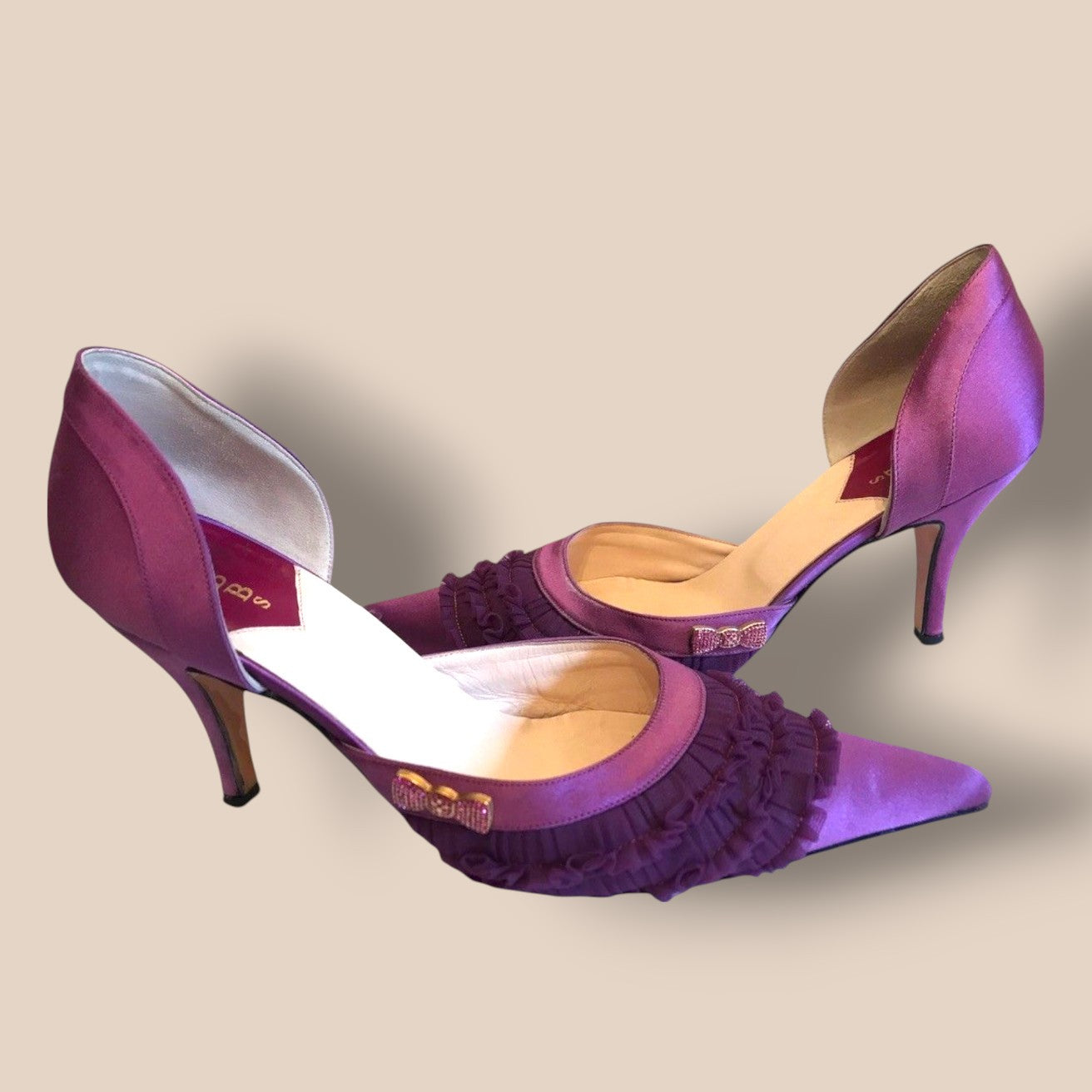 Purple high-heeled shoes with ruffled details on a beige background