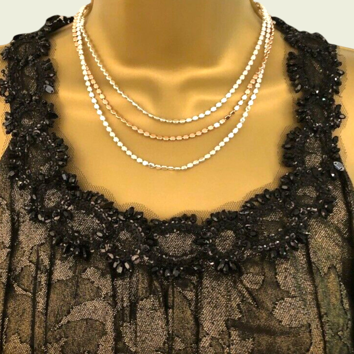 Mannequin wearing a black lace garment with gold necklaces.
