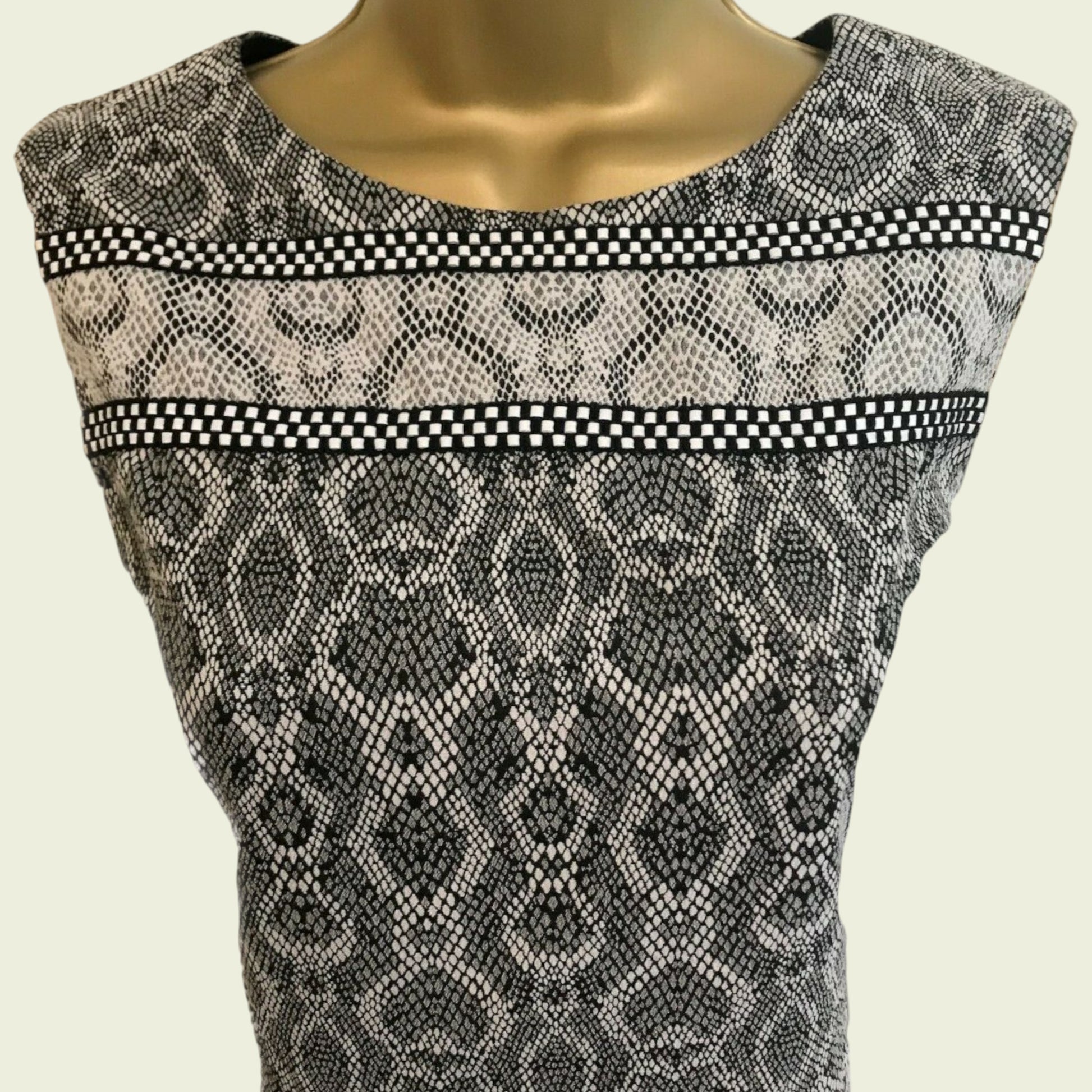 Mannequin wearing a sleeveless dress with snake print and checkered trim on a beige background
