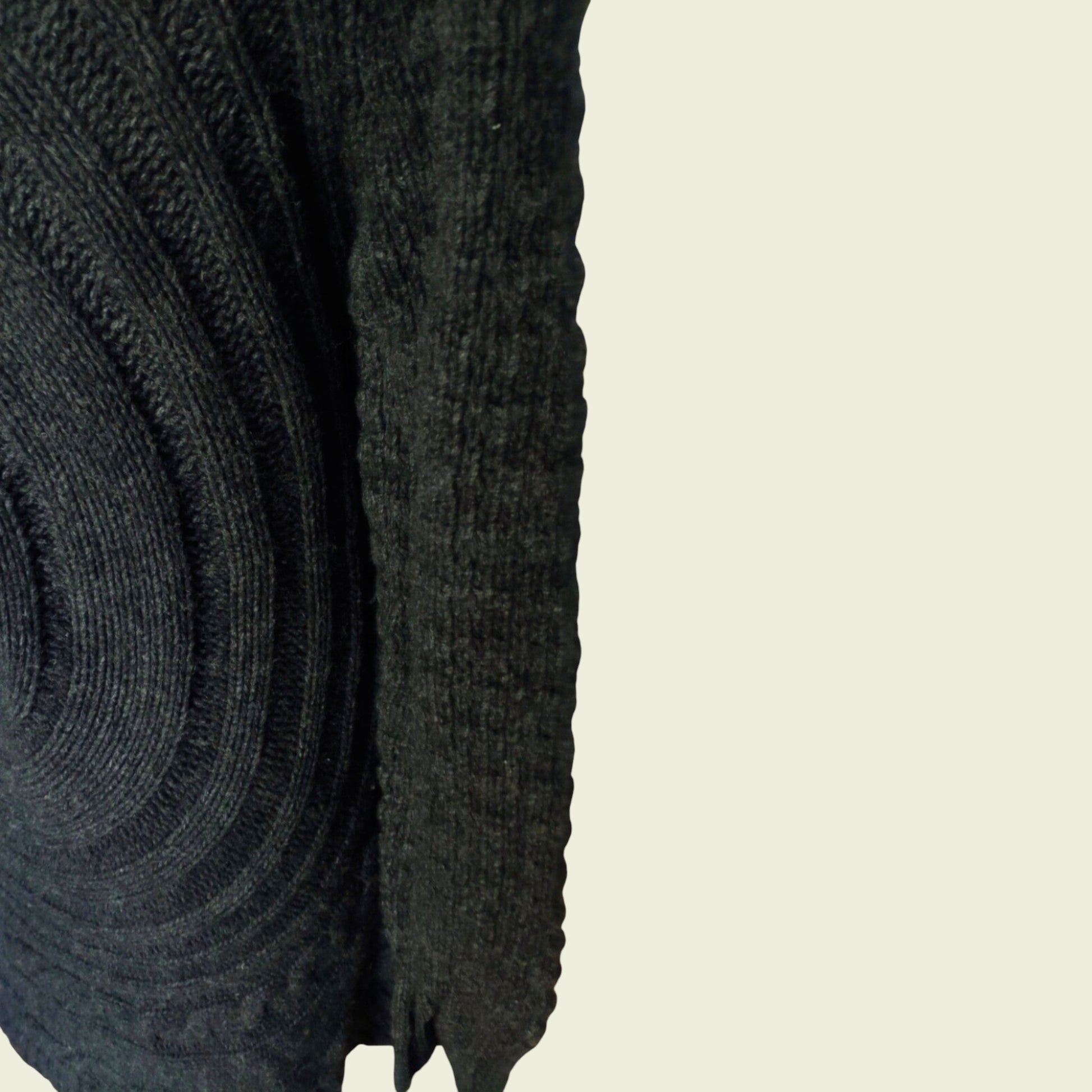 Close-up of a dark gray knitted sweater sleeve on a beige background