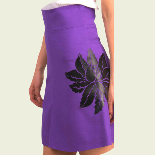 Model wearing purple skirt with black flower on beige background